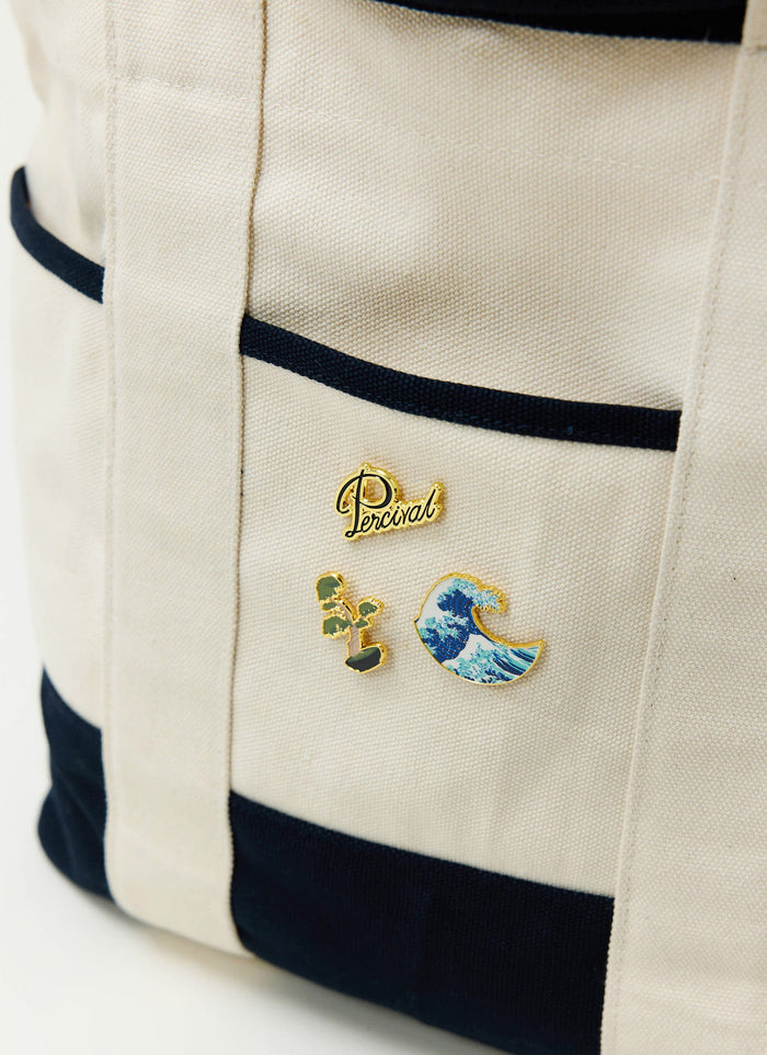 Three Percival pin badges, including a wave, a bonsai tree, and the Percival logo, are pinned to a cream canvas tote bag.