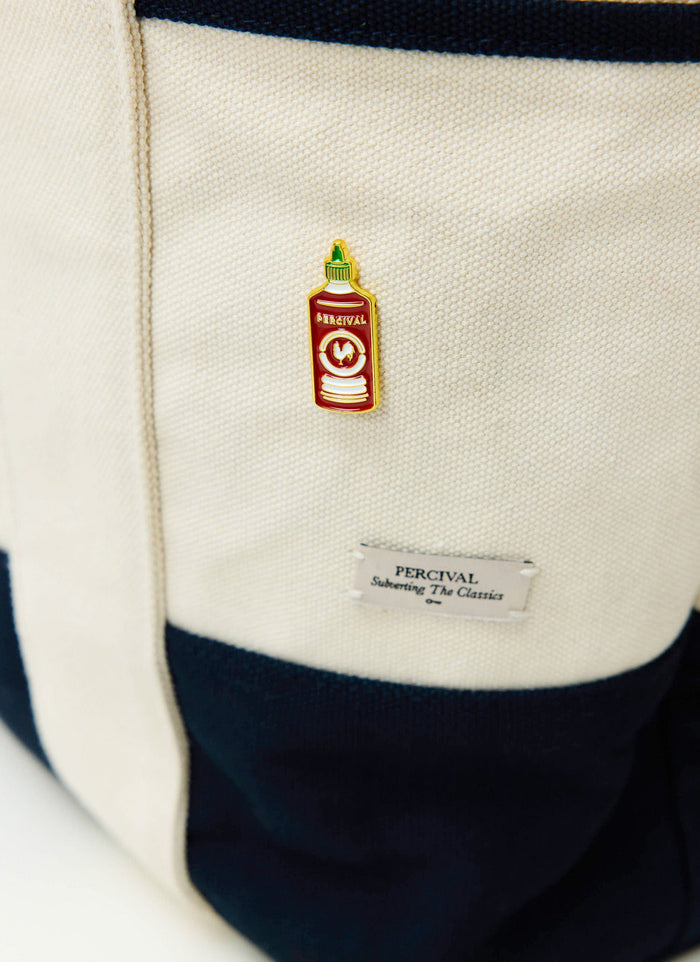 A close-up of the Percival Hot Sauce pin badge pinned to a cream and navy canvas tote bag.