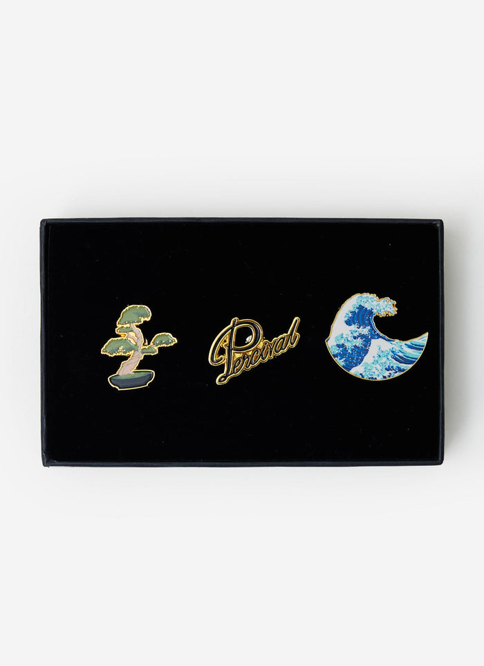 The Percival 3-pack of pin badges, featuring a bonsai tree, script logo, and wave designs, presented in a black gift box.