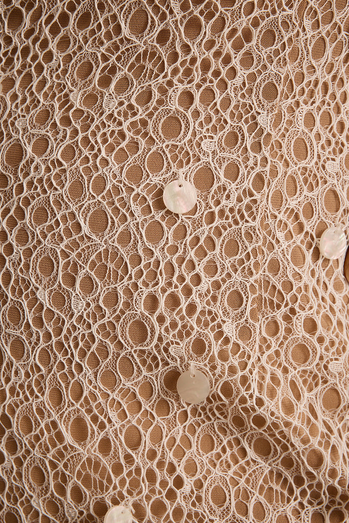 Close-up of cream crochet lace over tan lining with iridescent shell discs stitched throughout.