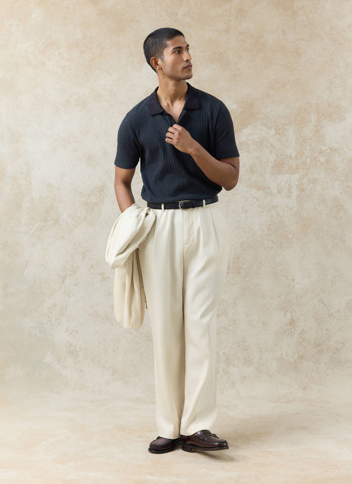 Black Percival Anthony Ribbed Polo in organic cotton, styled with cream pleated trousers and a blazer over the arm.