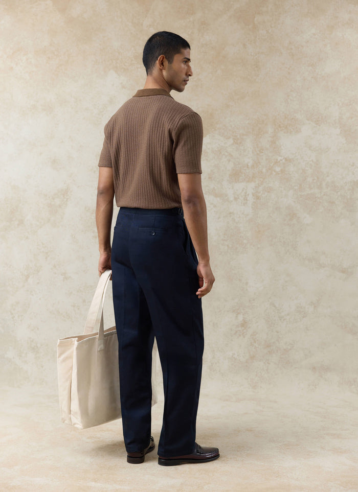 Rear view of a model wearing the Percival espresso ribbed polo and navy Blake double pleated cotton trousers.