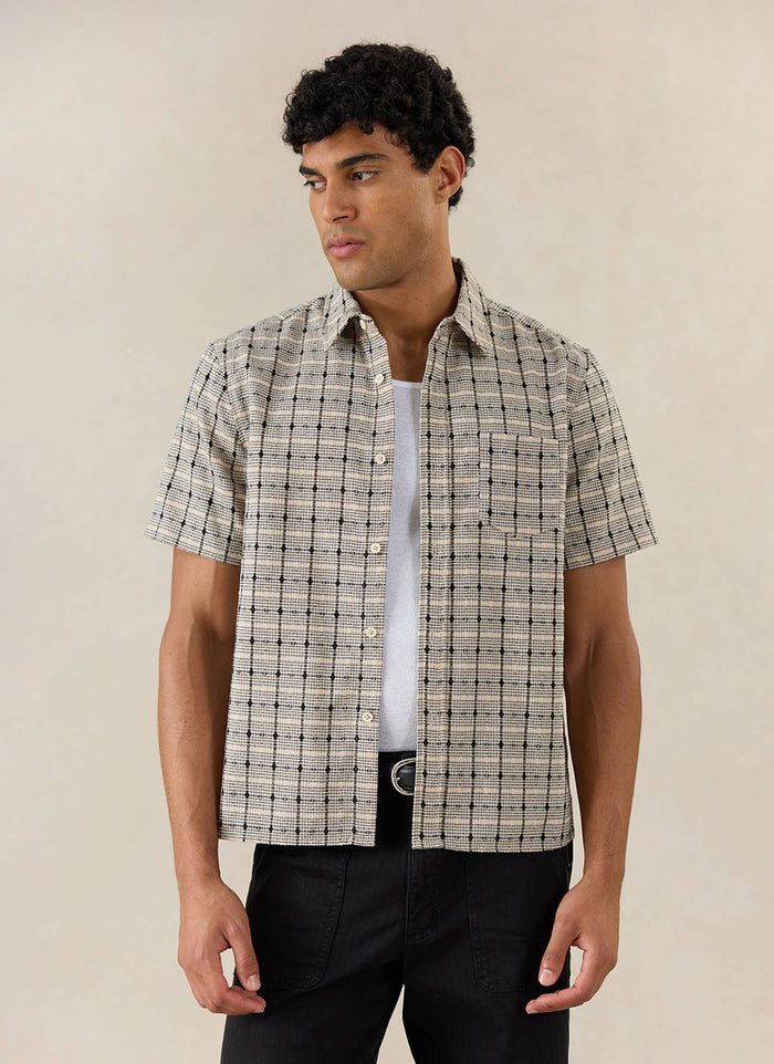 Model wears the Percival Bayley Textured Check Shirt in cream cotton, styled over a white tank top and black trousers.