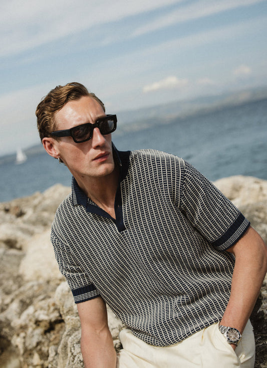 Percival Claude Knitted Polo in navy two-tone textured cotton, worn by a model in a scenic coastal setting.