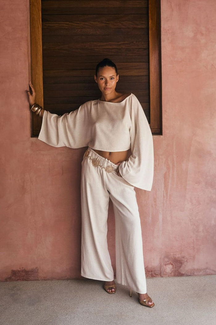 Cropped white linen bell-sleeve top styled with matching wide-leg linen pants against a pink stucco wall.