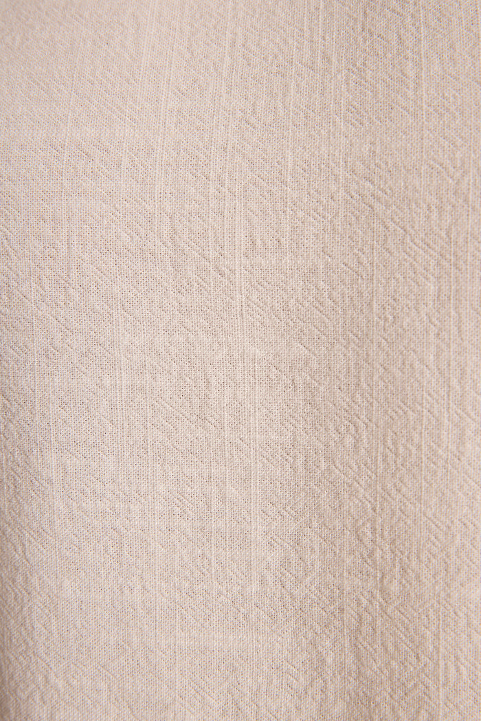 Close-up of textured cream linen fabric with a subtle geometric weave on a resort wear top.