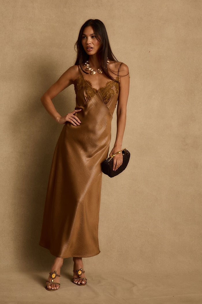 Bronze satin maxi slip dress with lace bust, styled with gold necklace and woven clutch.