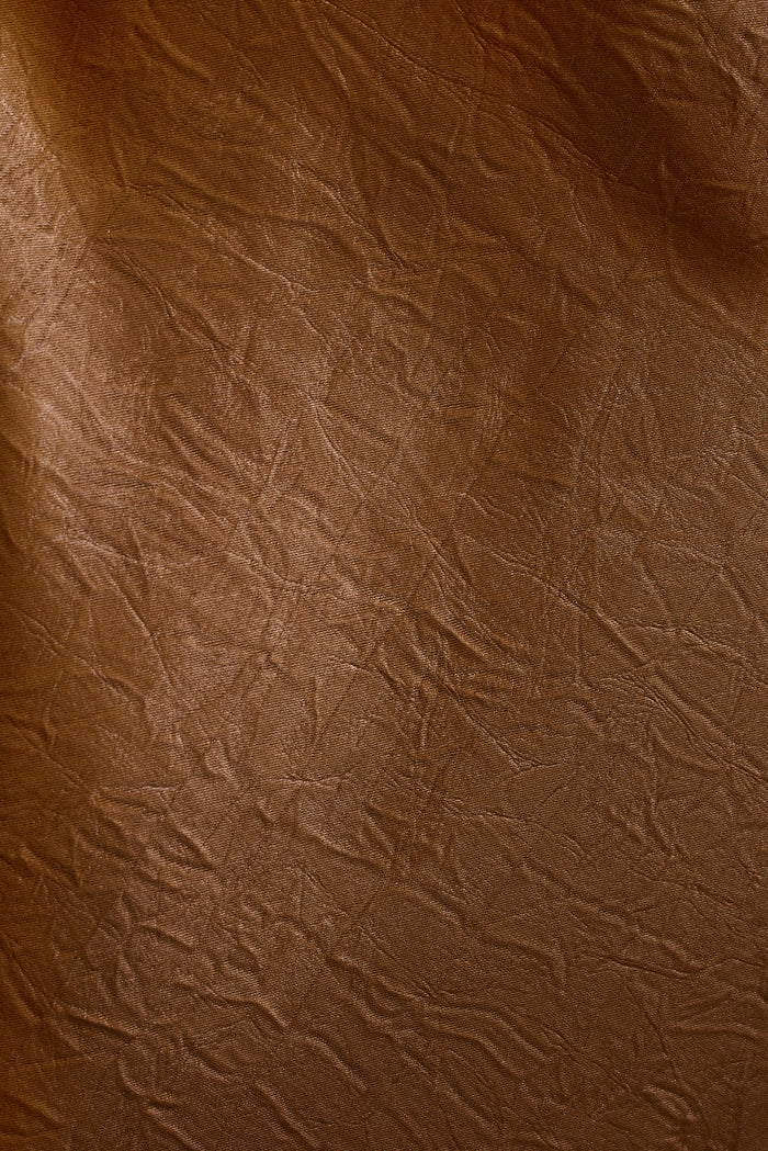 Close-up of crinkled bronze satin fabric from the Cordon maxi dress, catching soft light.