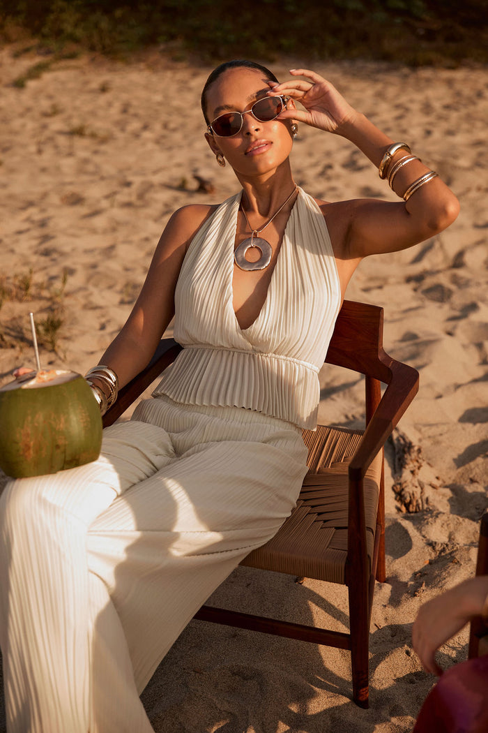 Cream plisse halter top with deep v-neckline, worn with matching wide-leg pants on a beach chair.