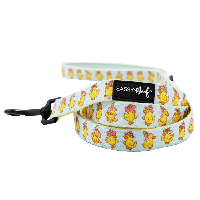 The Sassy Woof Dog Leash - Good Duck, Babe! features a light blue color with playful yellow ducks in pink bows, a secure black metal clip, and a comfortable neoprene handle with a stitched Sassy Woof label for added grip.