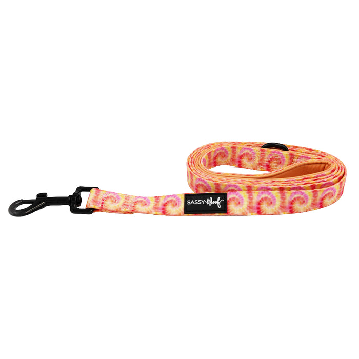 The Sassy Woof Dog Leash - Summer Sorbet features vibrant pink, yellow, and orange tie-dye, a padded handle for comfort, a black metal clip, and a Sassy Woof label.