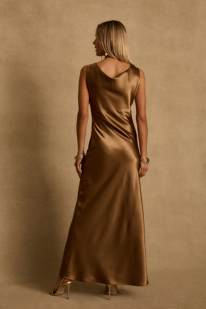 Back view of the bronze satin maxi dress with draped scoop back and gold heels.