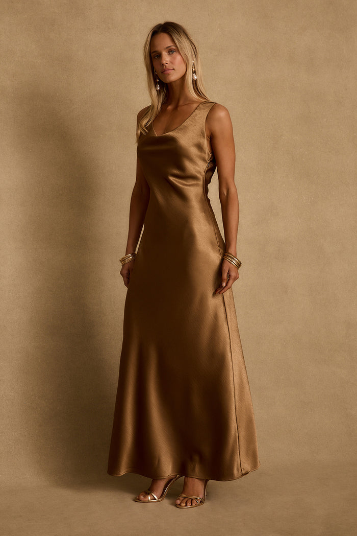 Bronze satin maxi dress worn with gold heels and bangles, styled as resort evening attire.