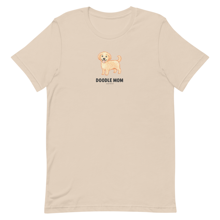 The Doodle Mom Tee by Sassy Woof is a beige unisex shirt featuring a small, smiling dog illustration above bold DOODLE MOM text—perfect for any proud Doodle mom.