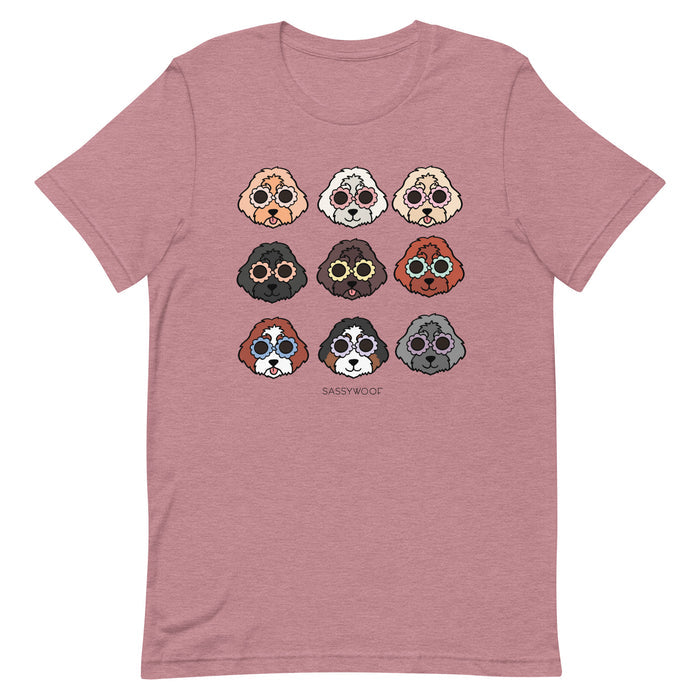 The Sassy Woof Doodle Tee is a mauve unisex t-shirt with nine cartoon dog faces in a grid and “SASSY WOOF” printed underneath. Made from 100% cotton for comfort.