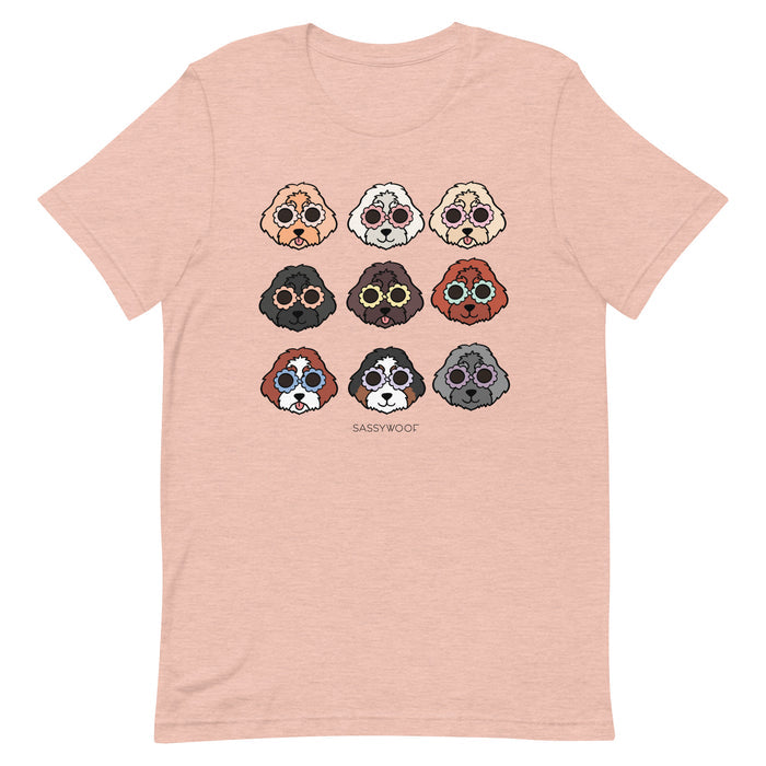 The Doodle Tee by Sassy Woof is a light pink unisex 100% cotton t-shirt with nine unique dog faces in three rows and "SASSYWOOF" printed below the playful illustrations.