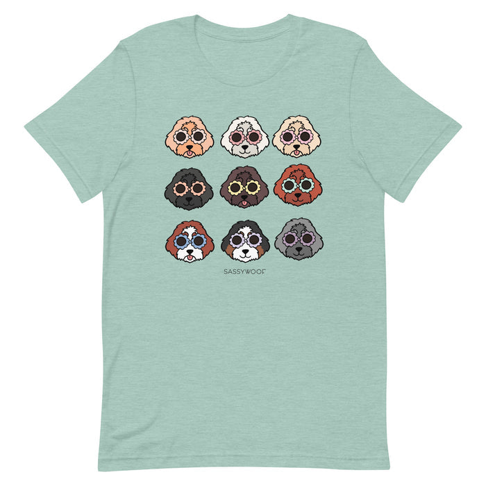The Doodle Tee by Sassy Woof is a light green unisex shirt with a grid of nine colorful dog faces and "SASSY WOOF" below, made from 100% cotton for comfort and style.