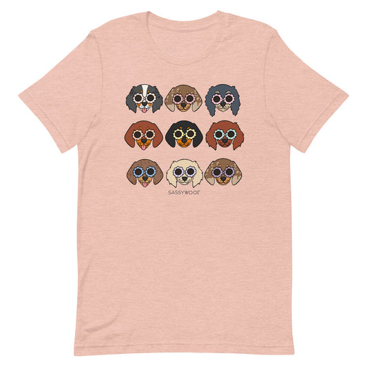The Sassy Woof Doxie Tee is a light pink unisex 100% cotton t-shirt with nine dogs in colorful sunglasses arranged in three rows above the SASSYWOOF logo, offering all-day comfort and playful style.