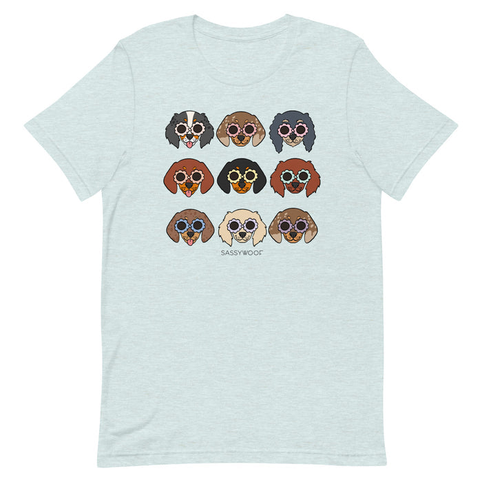 The Doxie Tee by Sassy Woof is a light blue unisex shirt with nine dogs in sunglasses, “SASSYWOOF” below, and made from 100% cotton for all-day comfort.