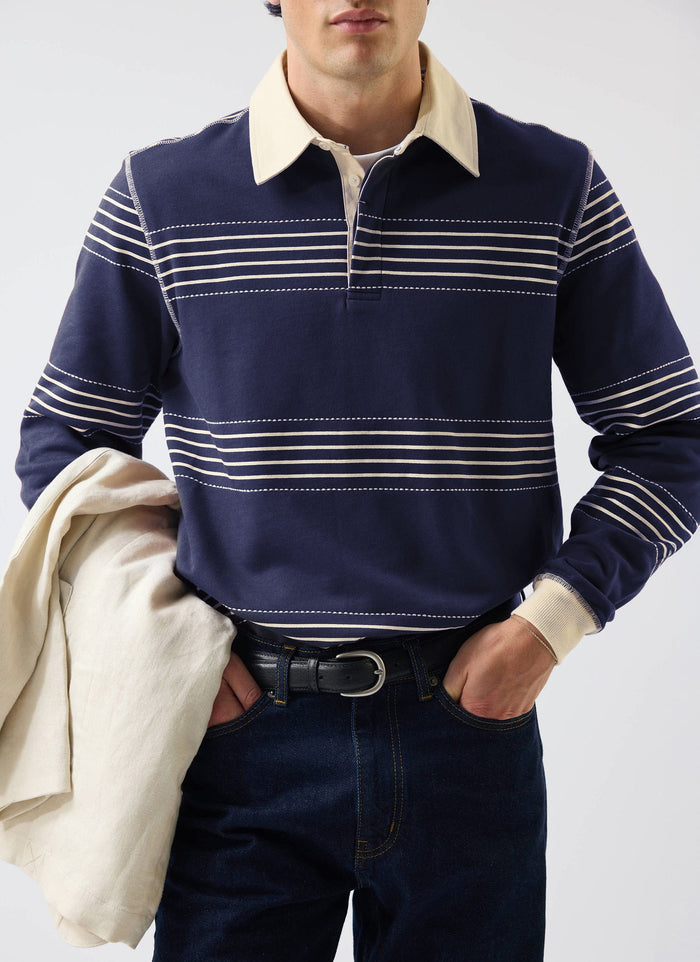 A close-up of a model wearing the Percival Editor Striped Rugby Polo Shirt in navy with its cream contrast collar.