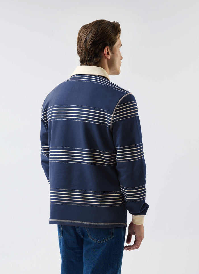 A model seen from the back wearing the navy Percival Editor Striped Rugby Polo, showing cream stripes and contrast collar.