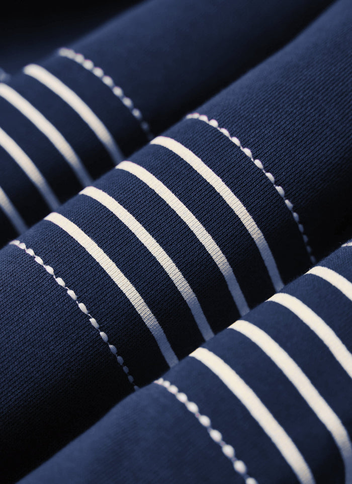 A close-up of the navy cotton Percival Editor Striped Rugby Polo Shirt, showing the cream stripe and stitch detail.