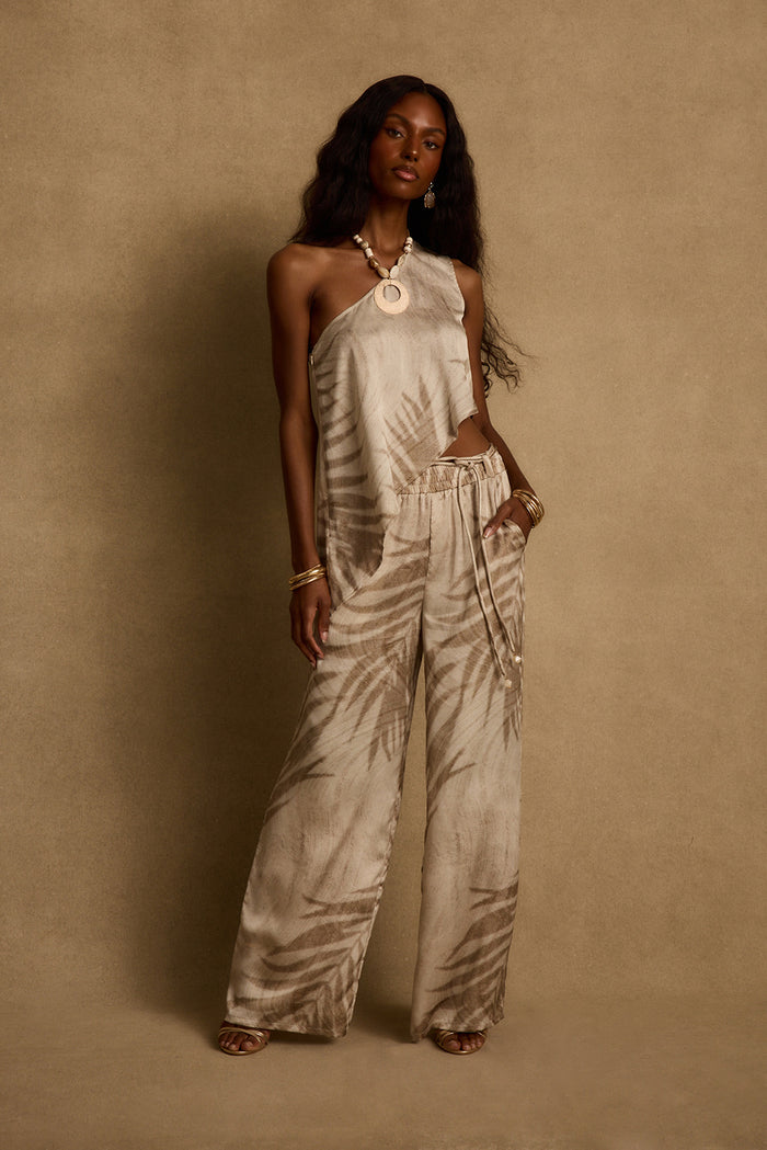 Estelle one-shoulder palm print top styled with matching wide-leg pants and gold jewelry.