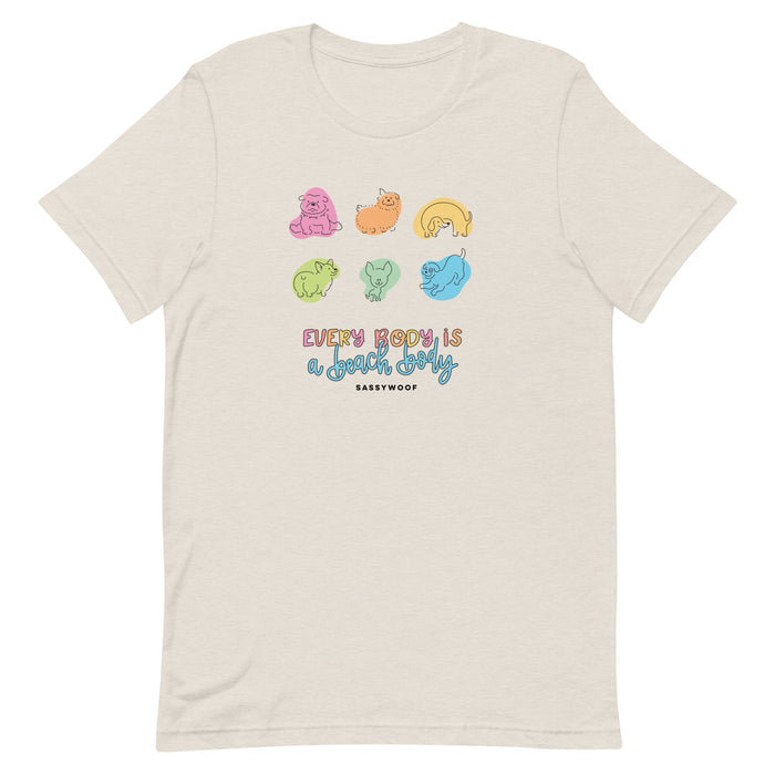 The Sassy Woof Every Body is a Beach Body Tee is a beige unisex shirt featuring colorful cartoon dogs above the text "Every body is a couch body" and "Sassy Woof" in black, offering comfort and style beyond the typical beach body tee.