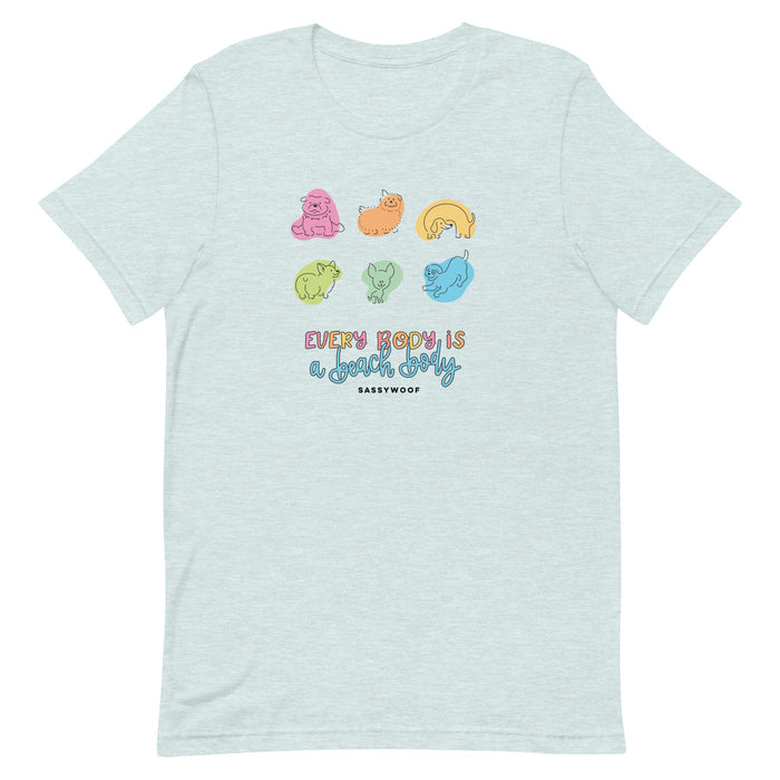 The Every Body is a Beach Body Tee by Sassy Woof is a light blue, lightweight t-shirt with colorful cartoon dogs and the messages “Every body is a good body” and “Sassy Woof.” Comfortable for everyone.