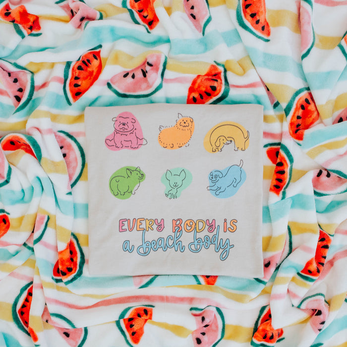 The Every Body is a Beach Body Tee by Sassy Woof is a light gray, comfortable, lightweight unisex shirt with cute cartoon dogs in various colors and poses above “EVERYBODY IS A BEACH BODY” in multicolored letters.
