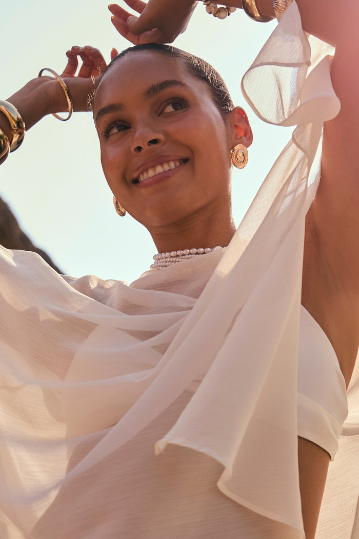Golden Dune textured gold coin earrings worn on-model with white chiffon and pearl choker.