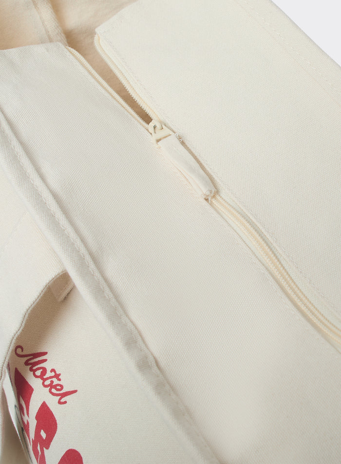 The Percival Gordon Large Tote Bag in cream cotton, showing a close-up of the zip closure and red graphic detail.