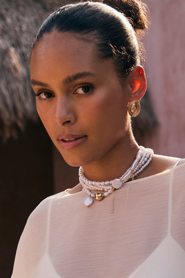Layered pearl and gold choker worn on-model with sheer ivory top in warm sunlight.