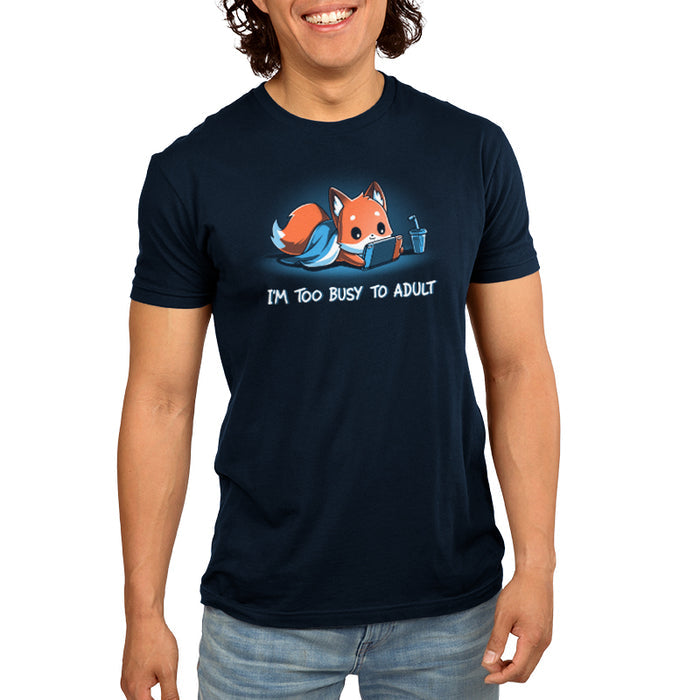 Premium Cotton T-shirt_TeeTurtle I'm Too Busy to Adult navy blue t-shirt featuring a fox lying down with a blue blanket, holding a video game tablet, next to a drink with a straw. Text below reads, "I'M TOO BUSY TO ADULT."
