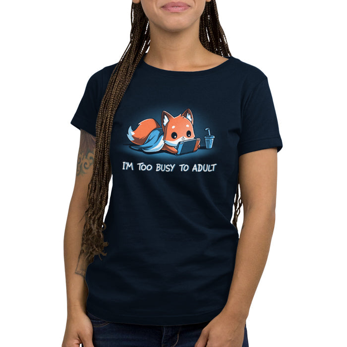 Premium Cotton T-shirt_TeeTurtle I'm Too Busy to Adult navy blue t-shirt featuring a fox lying down with a blue blanket, holding a video game tablet, next to a drink with a straw. Text below reads, "I'M TOO BUSY TO ADULT."