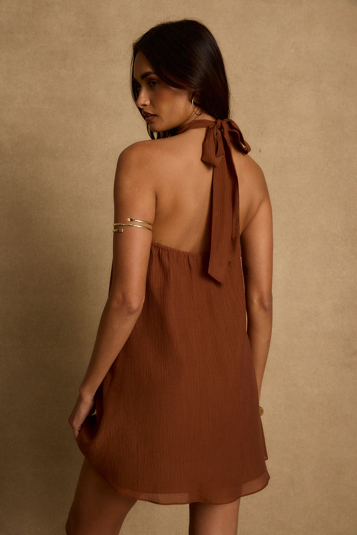Back view of the Iris terracotta halter tie mini dress with gold arm cuff.