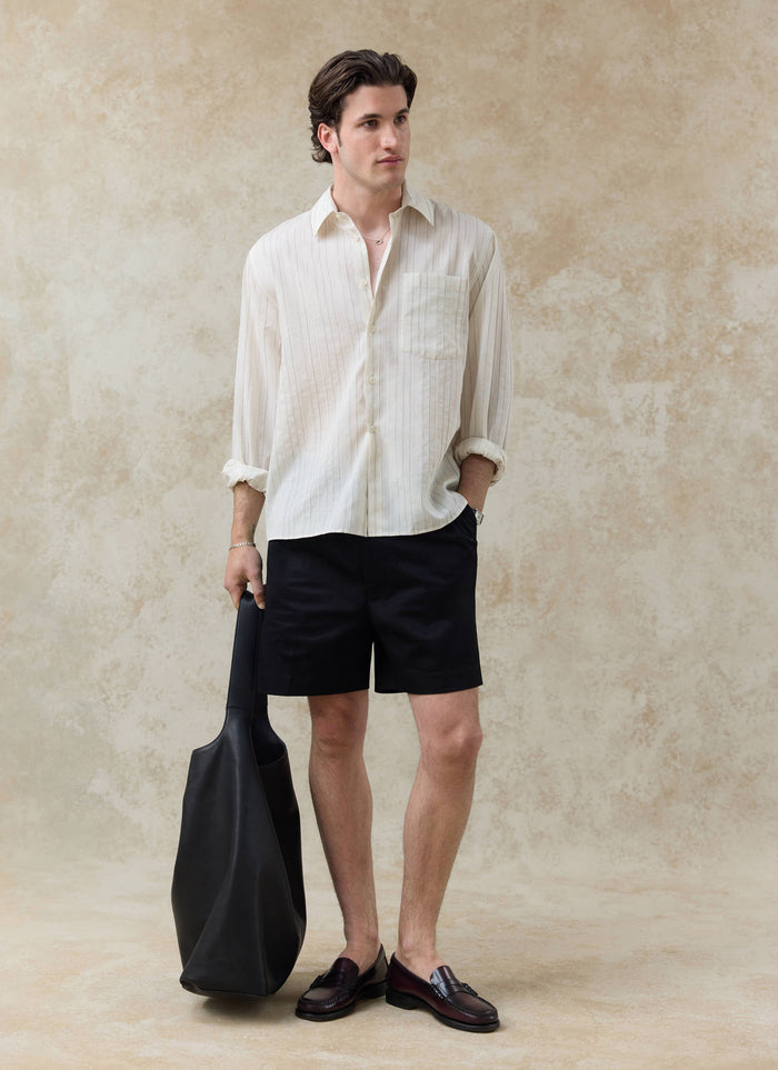 The Percival Lorenzo Pearce Shirt in cream stripe, a lyocell blend button-up styled with black shorts and a leather bag.