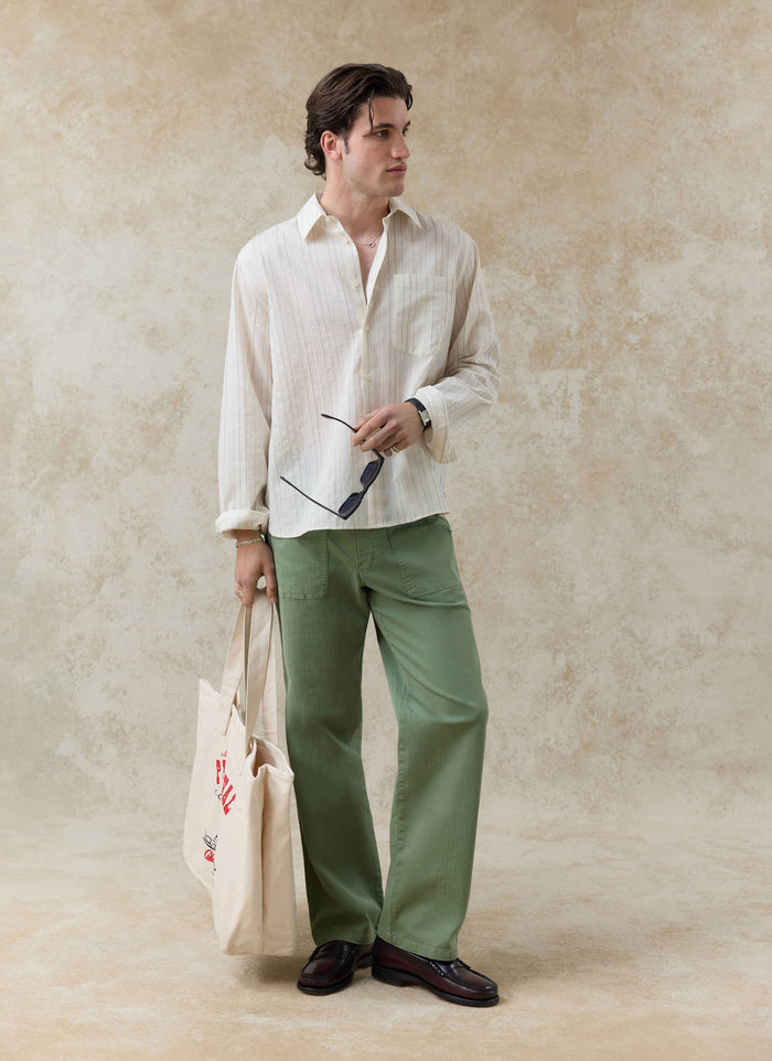 The Percival Lorenzo Pearce Shirt in cream stripe, a lyocell blend button-up styled with green trousers and a tote bag.