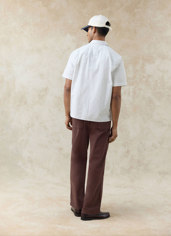 Rear view of a model wearing the Percival Lucia Embroidered Shirt in cream stripe cotton, styled with brown trousers.