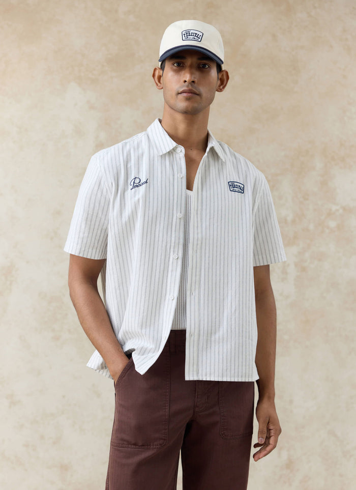 Model wearing the Percival Lucia embroidered cream stripe shirt and Donovan soft trucker cap with contrast navy peak.
