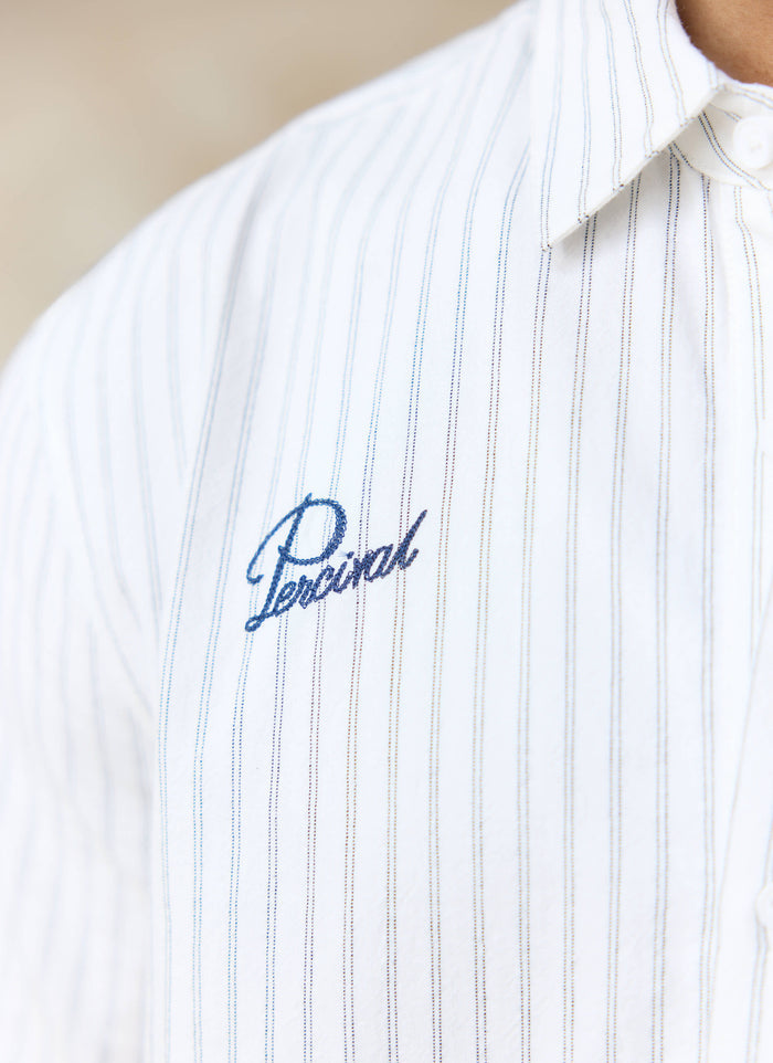 Close-up of the blue script Percival embroidery on the chest of the cream stripe cotton Lucia shirt.