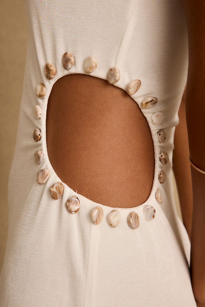 Hand-sewn stone beads outline the side cutout on a white cutout maxi dress.