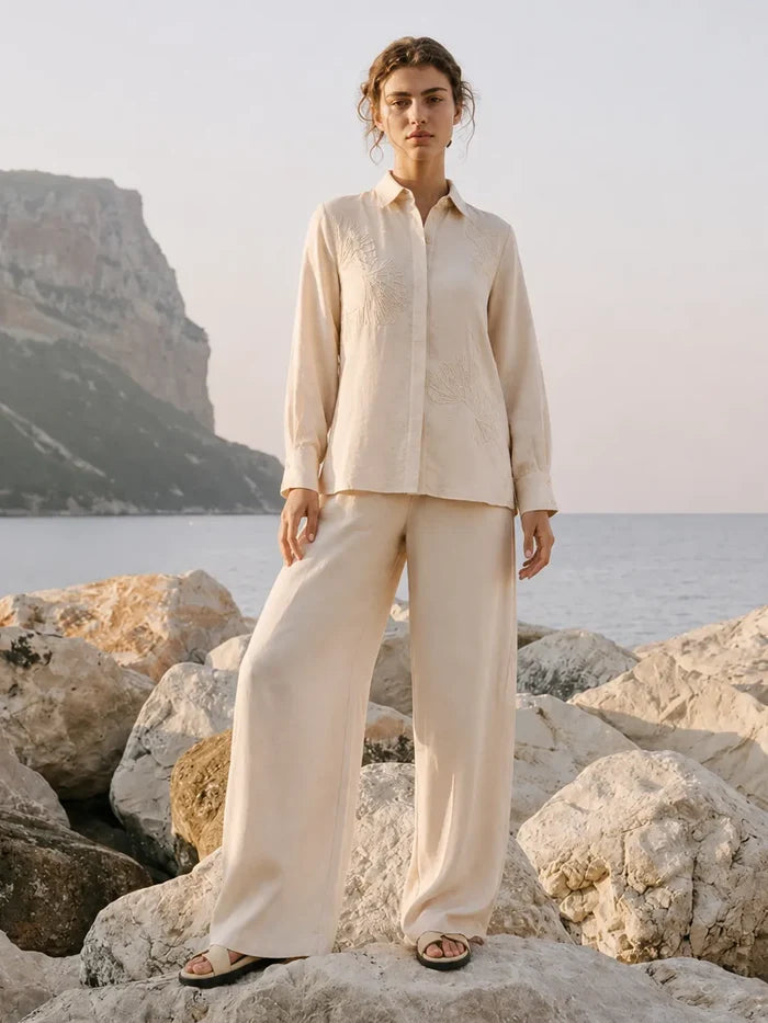 Person wearing a beige outfit standing on rocks by the sea