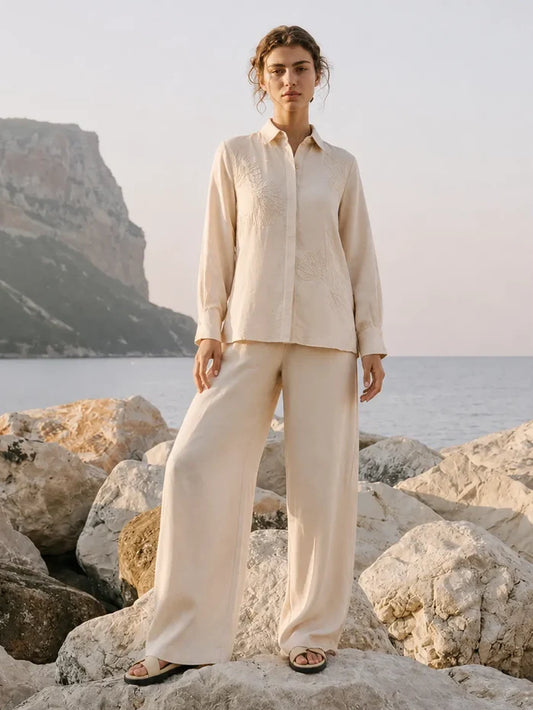 Person wearing a beige outfit standing on rocks by the sea