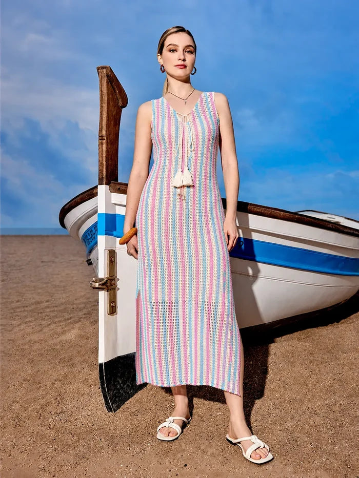 Woman in a striped dress standing next to a small boat on a beach.