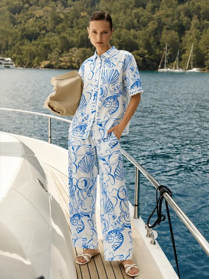 Woman in a blue and white patterned outfit standing on a boat with water and trees in the background