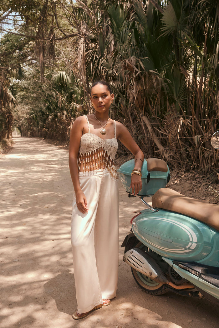 Cream crochet beaded fringe crop top styled with wide-leg trousers beside a turquoise scooter.