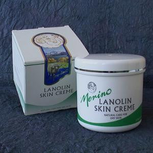 Merino 100g Lanolin Skin Crème with branding on a blanket next to its packaging box.