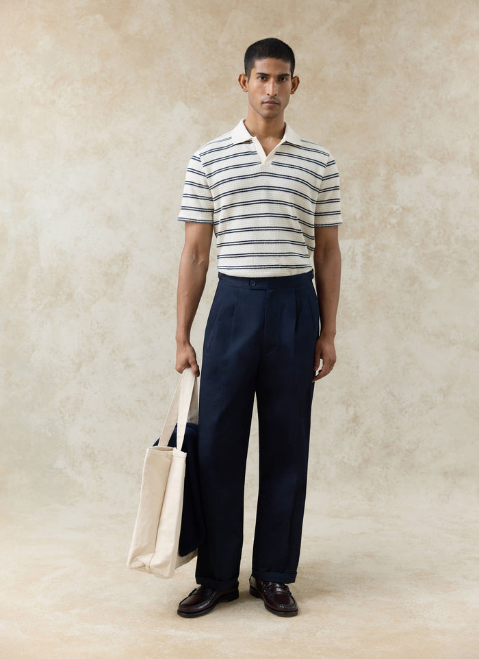 Percival Moore Polo in cream textured cotton with black stripes, paired with navy trousers and a canvas tote bag.