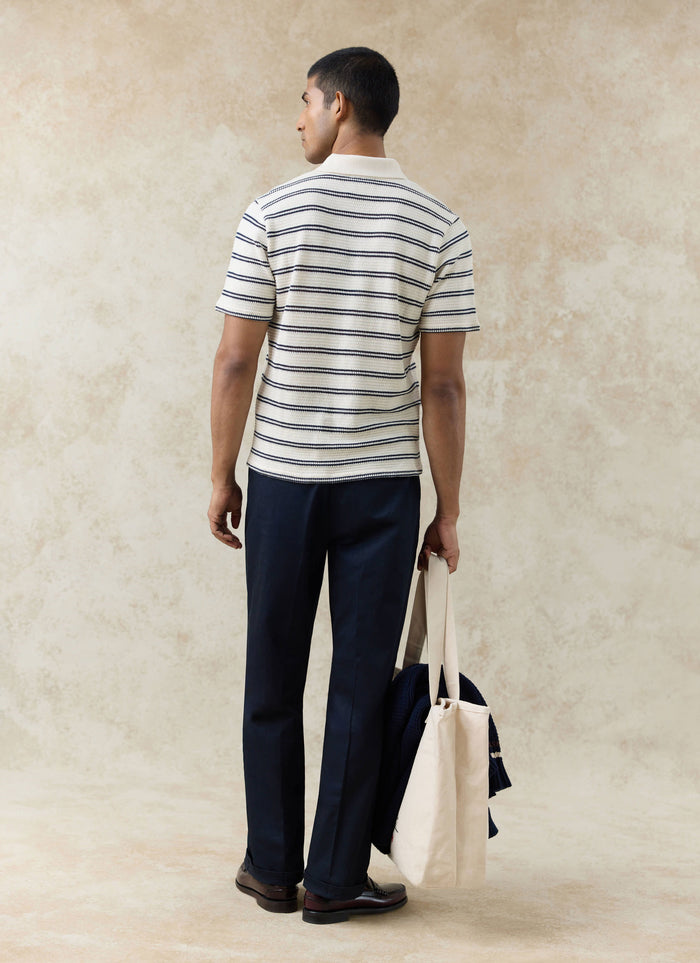 Rear view of the Percival Moore Polo in cream textured cotton knit with black stripes and navy trousers.